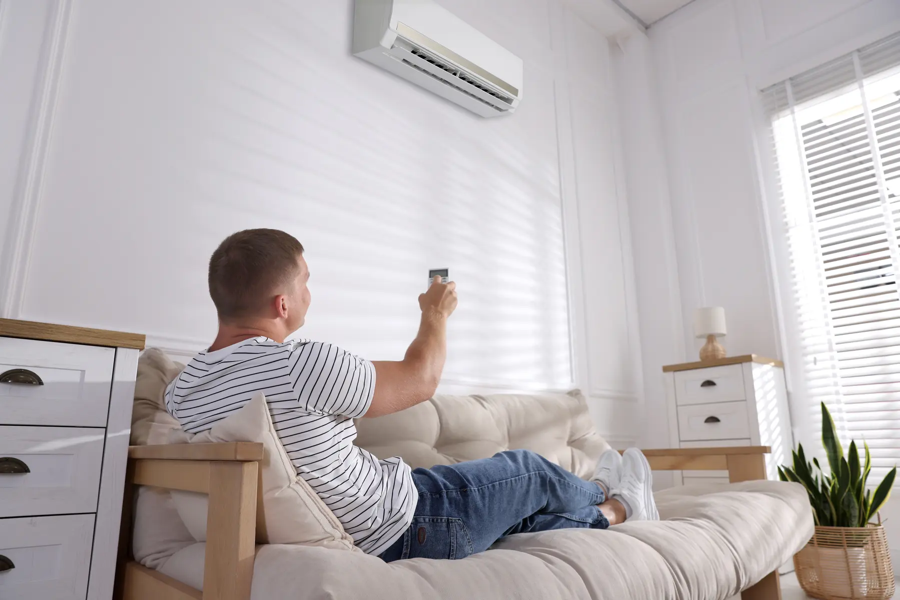 Homme pilotant sa climatisation murale avec une télécommande depuis son canapé dans un salon lumineux à Hyères les Palmiers.