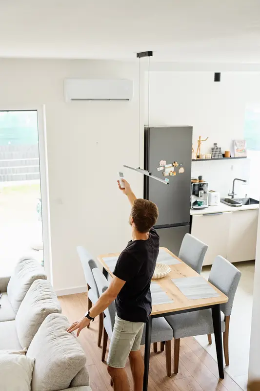 Homme réglant sa climatisation murale réversible via télécommande dans une villa moderne au Lavandou.